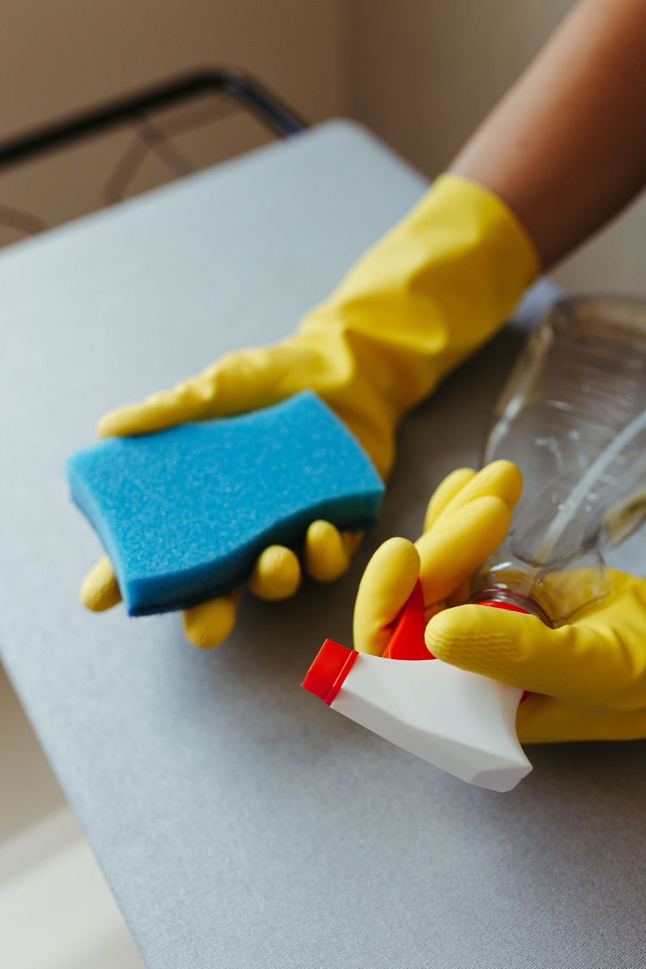 Cleaner holding a sponge and spray bottle while cleaning a surface