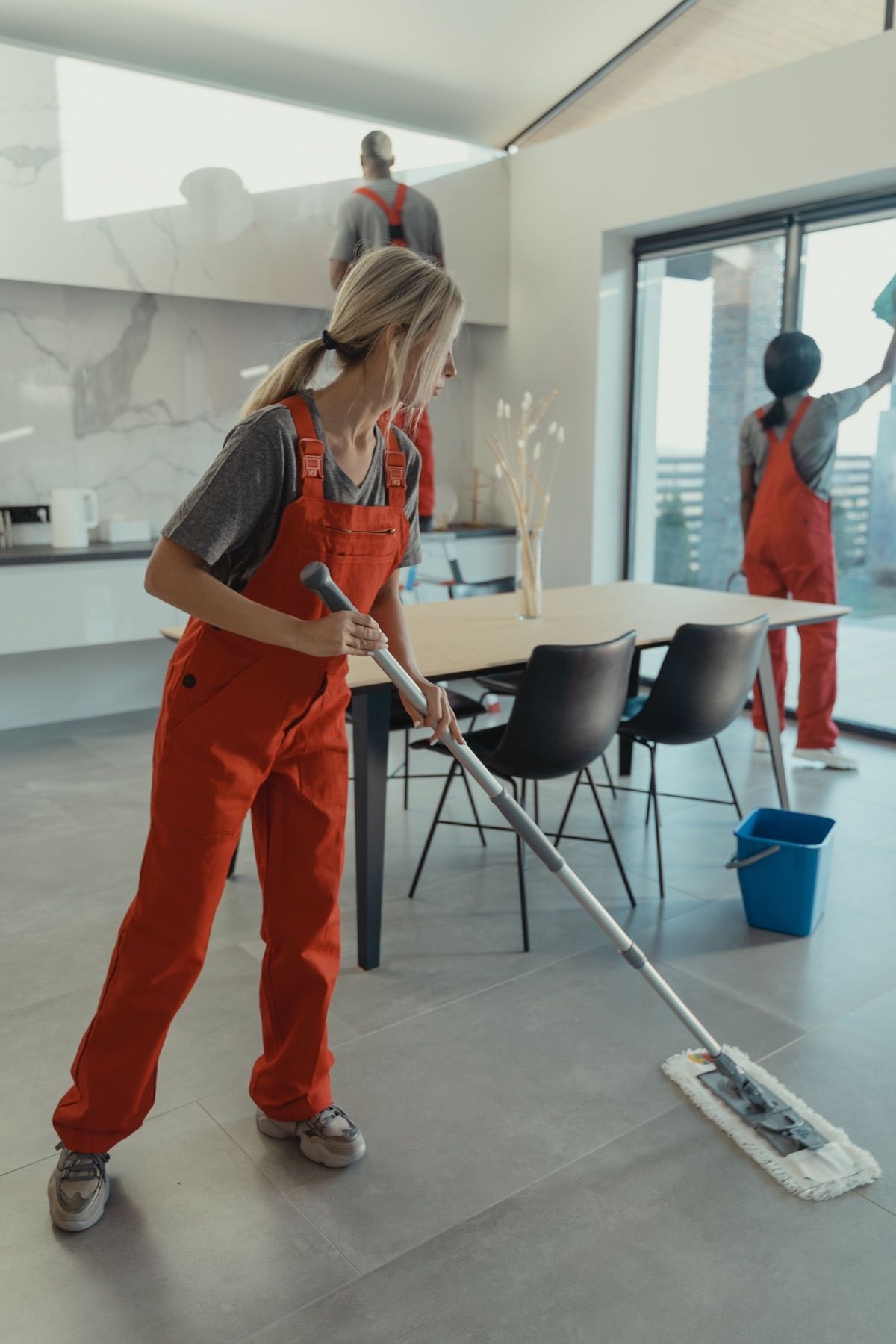 Super Cleaning employee mopping a tiled floor in a bright open-plan home