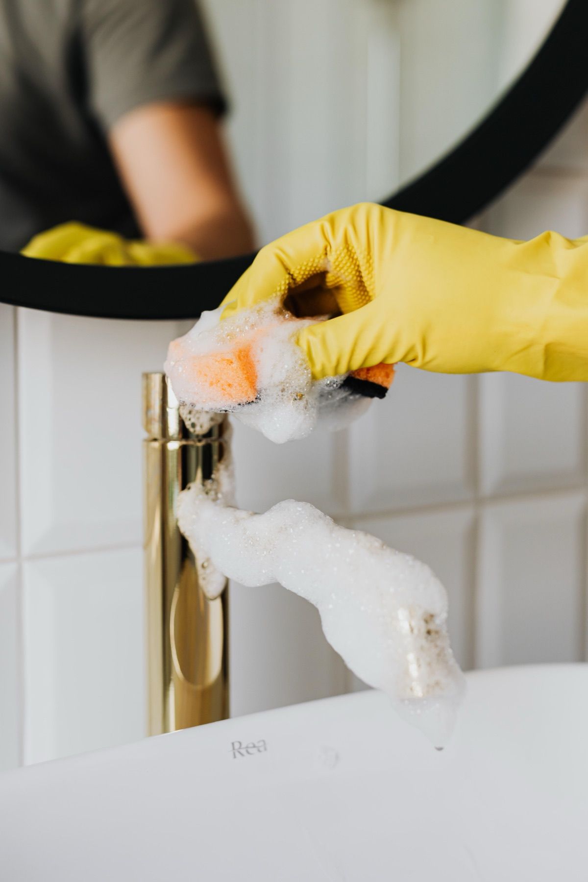 Gloved hand cleaning limescale from a bathroom tap with foam